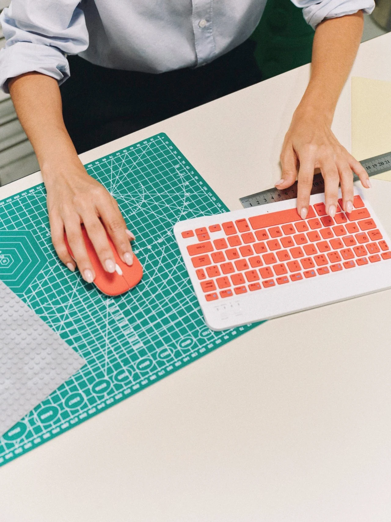 Hands at a red keyboard and mouse on a green cutting mat