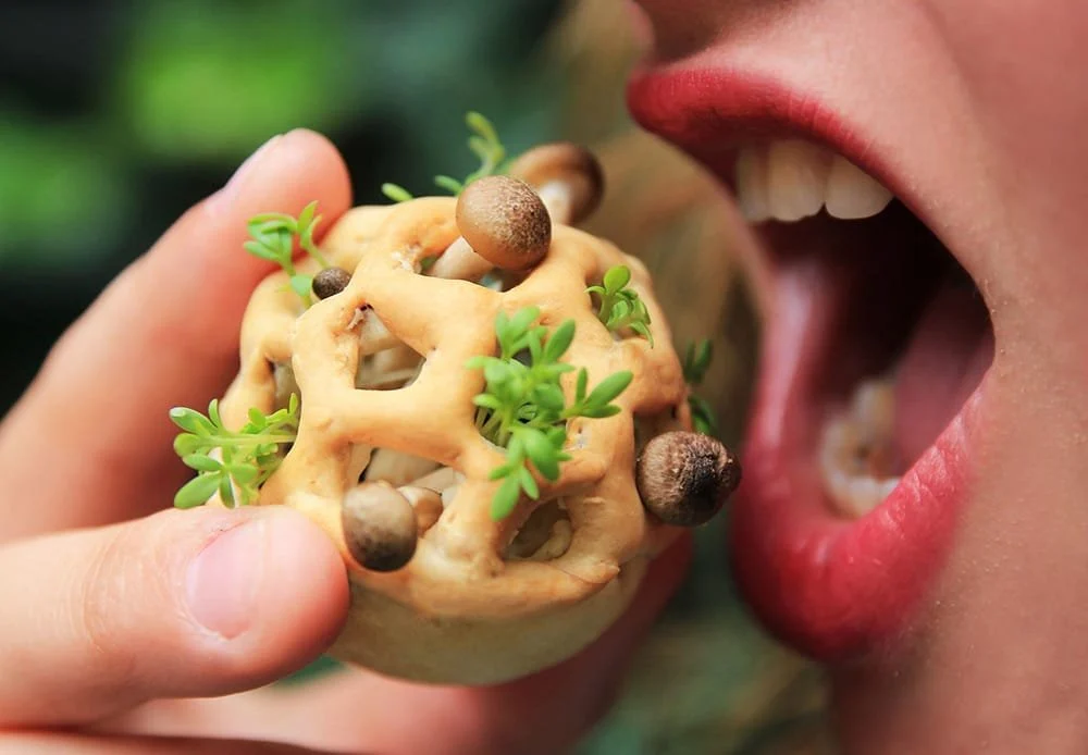 A hand holding a mushroom-topped biscuit up to an open mouth