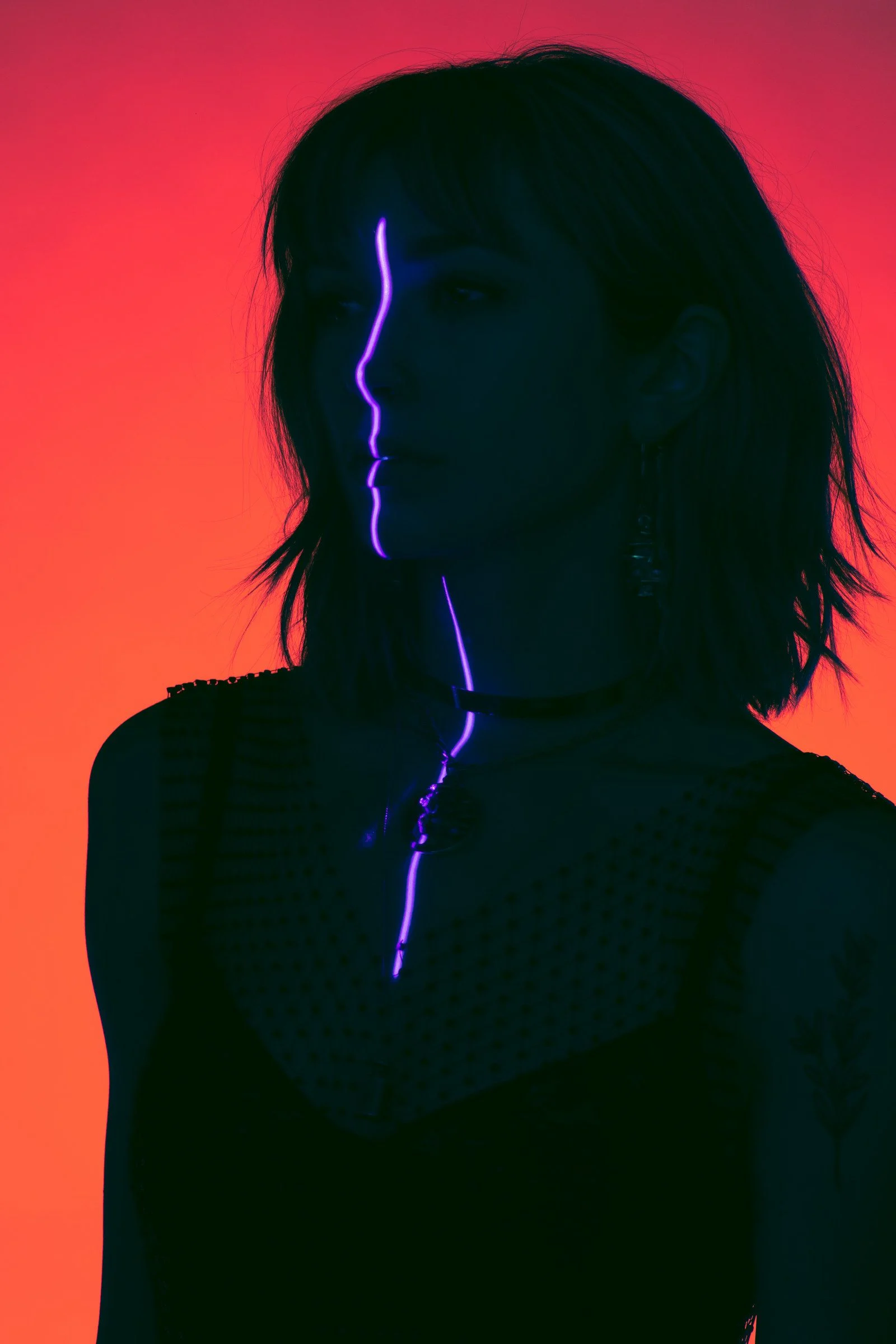 Woman in silhouette against a red background, a violet line of light down her face