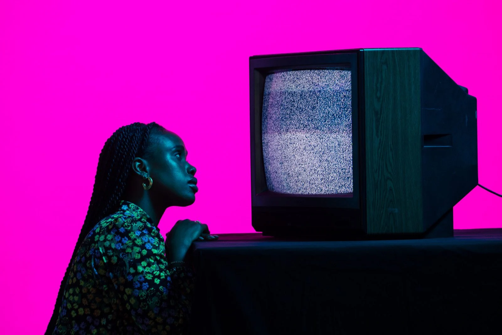 Woman watching a static-filled television against a bright pink background