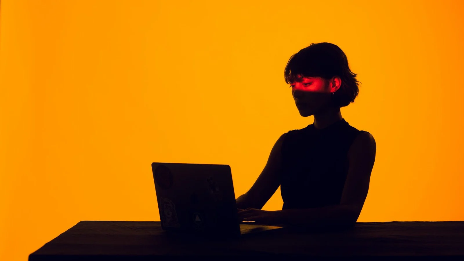 Silhouette of a woman working at a laptop against an orange background