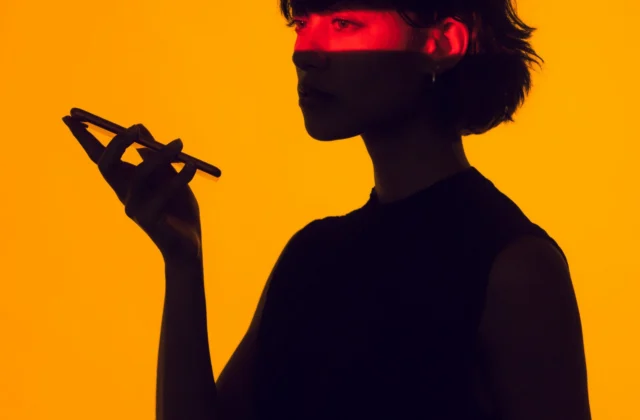 Silhouette of a woman holding up a phone against an orange background