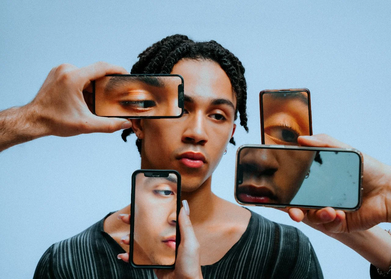 Young man surrounded by hands holding phones up to his face