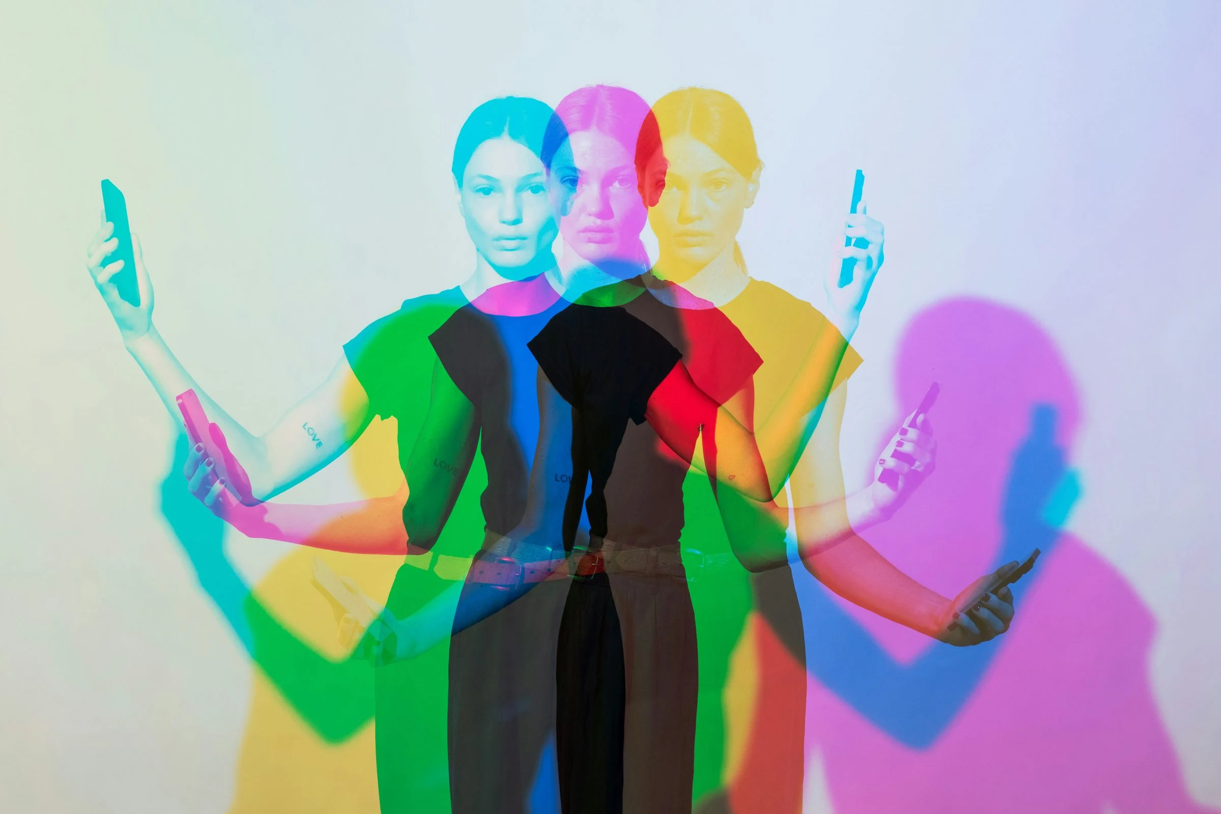 Woman holding phones, shown as overlapping red, green and blue copies of herself