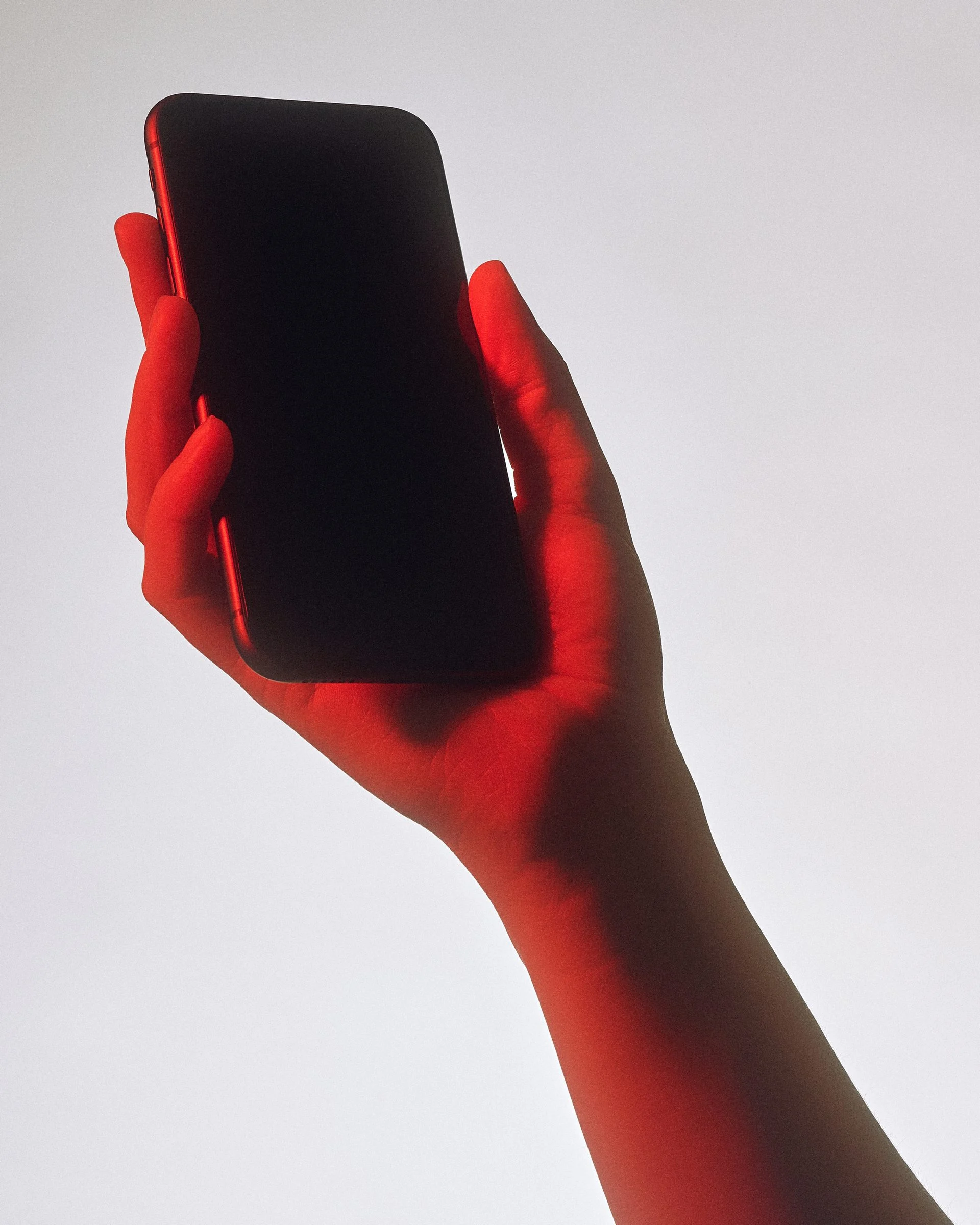 Hand holding a phone up against a white background, lit red