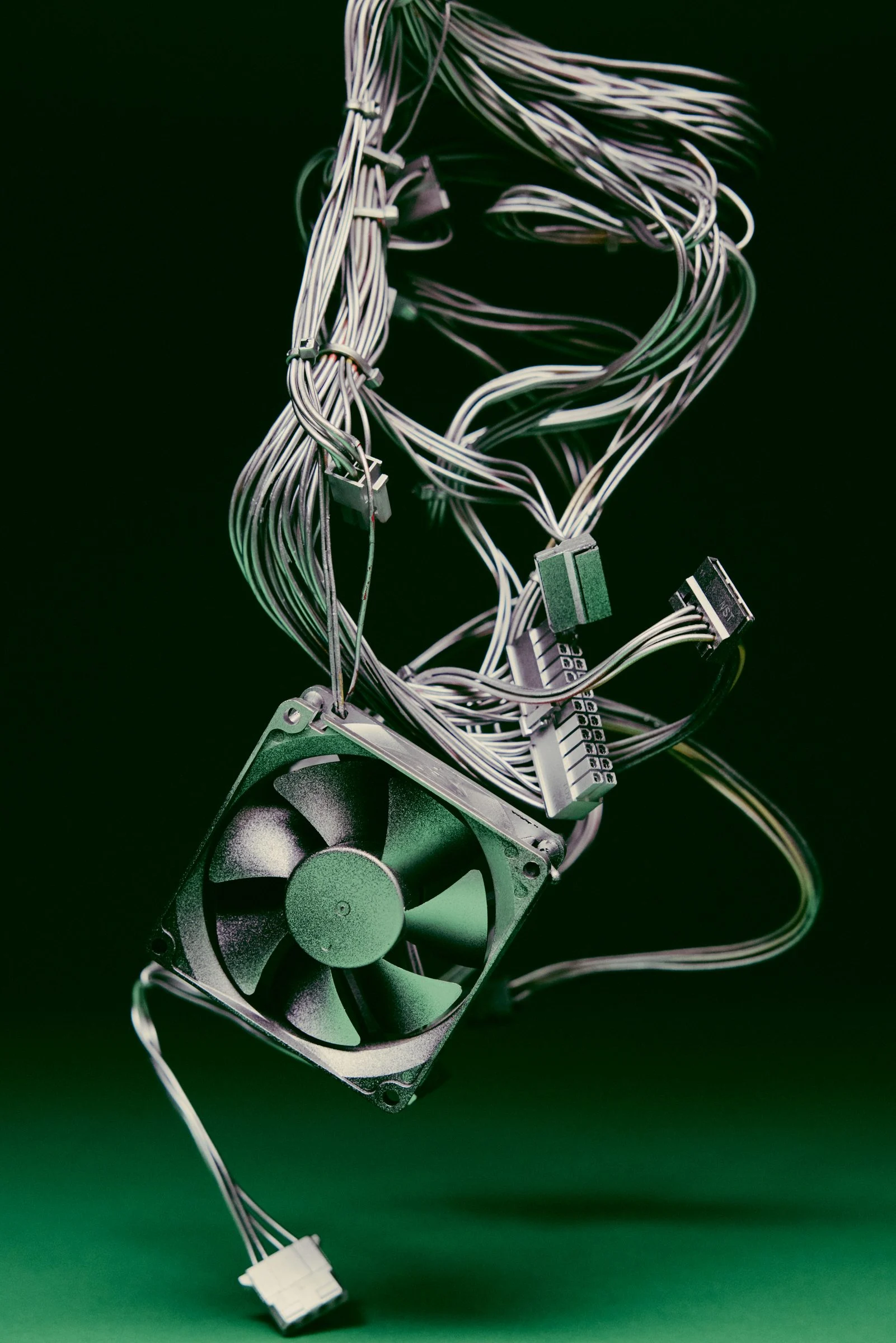 Tangle of cables and a cooling fan suspended against a dark green background