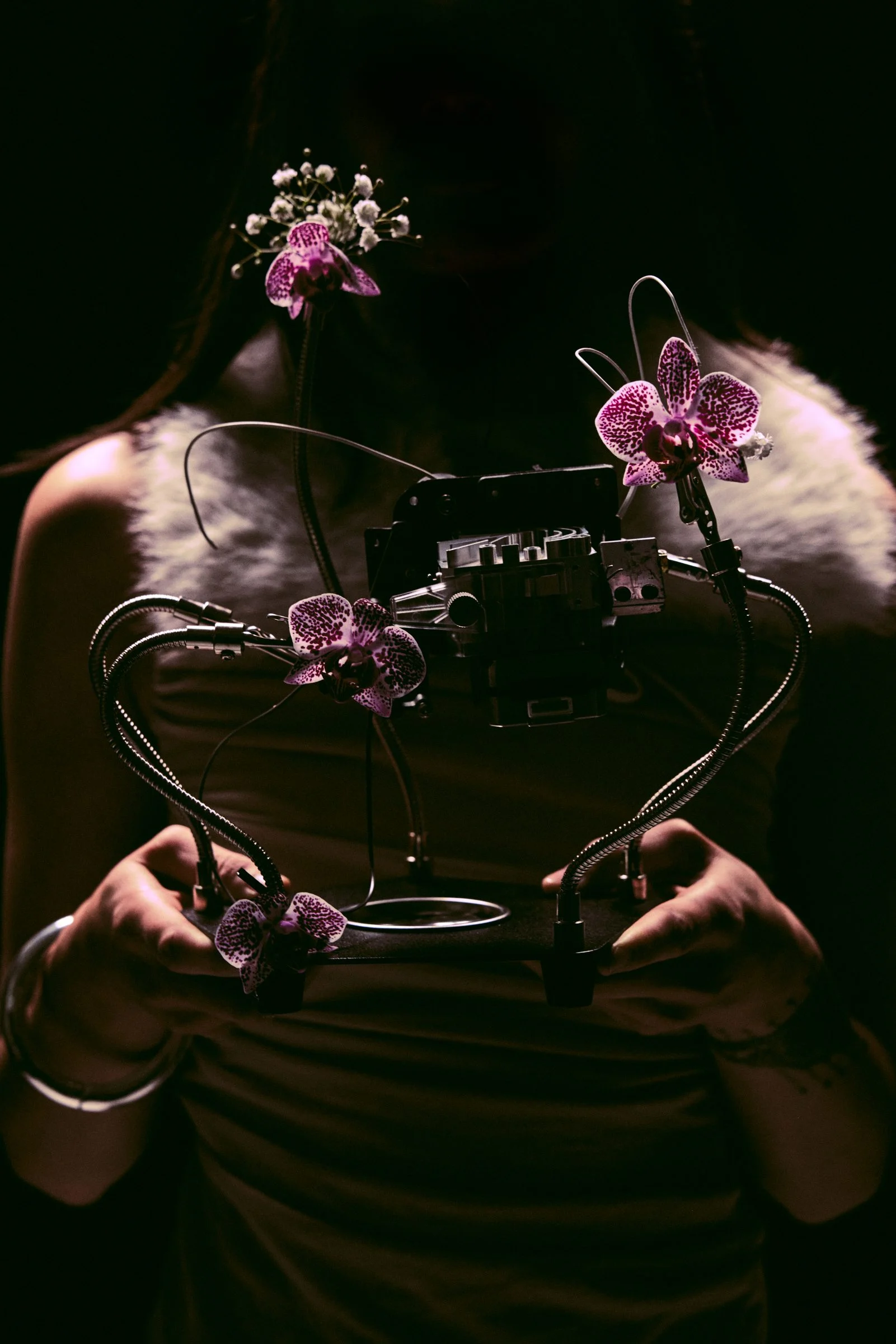 Hands holding a sculpture of metal arms and pink orchids