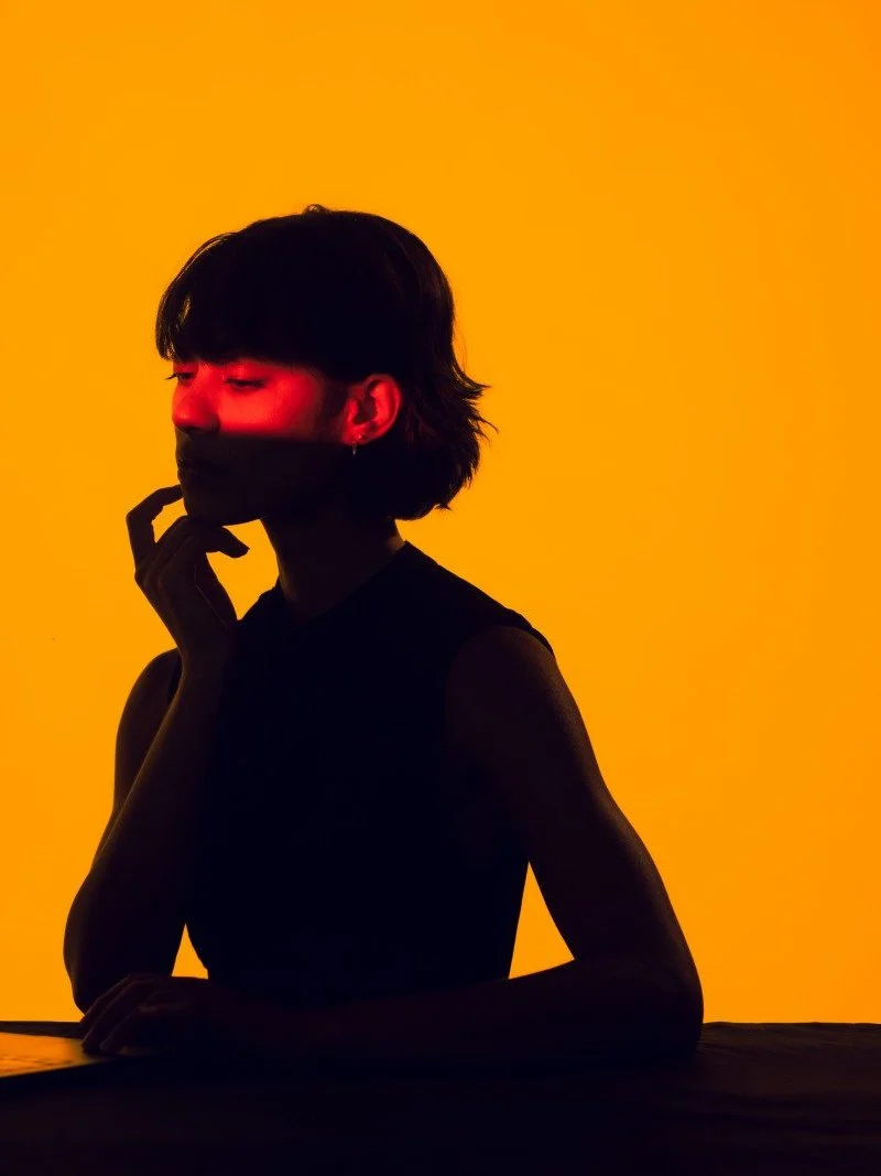 Silhouette of a woman against an orange background, a band of red light across her eyes